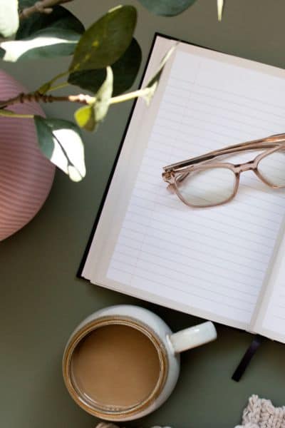 notebook with a set of glasses on it and a cup of coffee next to it.